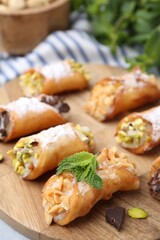 Delicious cannoli with cheese, nuts, powdered sugar, chocolate and mint on table, closeup