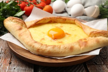 Tasty khachapuri with cheese, egg and other products on wooden table, closeup