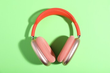 Pair of stylish pink headphones on light green background, top view