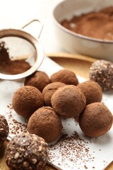 Tasty chocolate candies with cocoa powder and strainer on light table, closeup