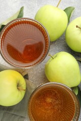 Delicious cider in glasses, apples and leaves on grey textured table, flat lay