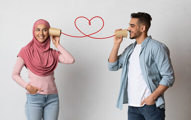 Romantic arab guy sending love message to muslim girlfriend through paper cup phone connected by...