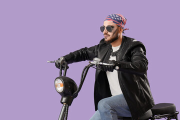 Young man dressed as biker for Halloween riding electric bike on purple background