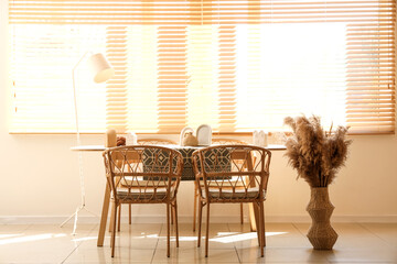 Interior of dining room with table, chairs, lamp and dry flowers in vase near window