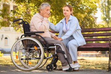 Upset senior woman in wheelchair with caregiver outdoors