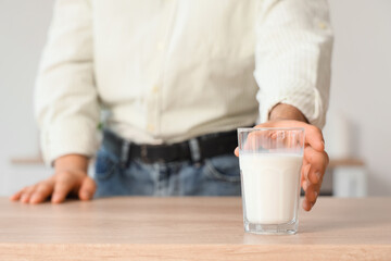 Young man taking glass of milk from table in kitchen, closeup