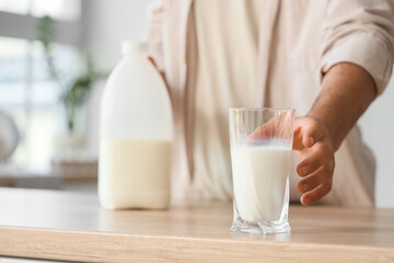 Young man taking glass of milk from table in kitchen, closeup