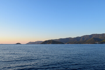 Beautiful island landscape at sunset with lush, thick woodland and turquoise tropical waters. Mountains, dense green forests, white rocks and clear blue waters make up the idyllic travel destination.