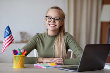 Cute teen girl with USA flag using laptop, studying american english online from home, copy space....