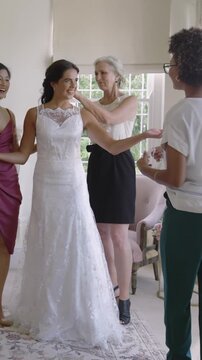 Vertical video: Diverse group smoothing lace gown and adjusting sandals after bride smiles at salon