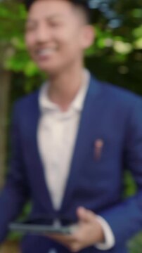 Vertical video: Diverse wedding party sharing vows as officiant reading on tablet under draped arch