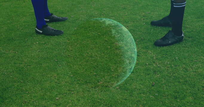 Holographic orb hovering between soccer players standing on pitch, wearing soccer socks and cleats
