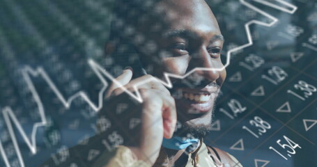 Smiling finance professional holding smartphone to ear in office, with digital stock charts