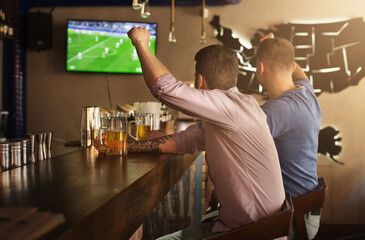 Two friends watching football game and drinking beer at the pub