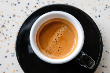Top view of a freshly brewed espresso served in a black cup on a wooden table with terrazzo background. Perfect for cafe branding, restaurant, coffee shop promotions, and espresso culture, barista