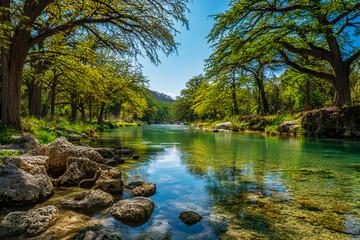 The Guadalupe River in the spring, blue water, green trees, rocks on the shore, clear sky, professional photography in the style