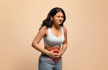 Sick young indian woman having stomach ache, touching her abdomen with red inflamed zone, eastern...