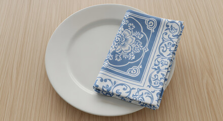 A white plate with a folded blue and white patterned napkin on a light brown wooden surface top view