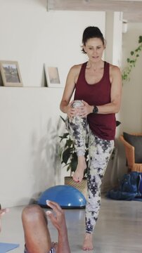 Vertical video: On trainer's cue, trainer is adjusting client's raised leg on mat for alignment