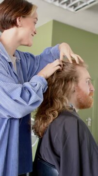 Vertical video: Female stylist in 20s placing tips on scalp, sliding hair, assessing hair in salon