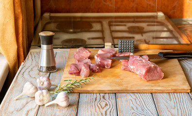 Fresh raw pork meat prepared on cutting board with garlic, rosemary, and kitchen tools, ready for...