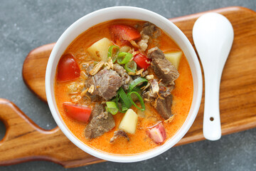Top view of a delicious bowl of Soto Betawi, highlighting the combination of tender beef, tomato, potato chunks, and a thick, creamy soup, garnished with spring onions.