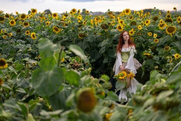 Redhead woman in flowing gown gazes skyward amidst a vibrant field of sunflowers, holding a woven...