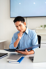 Naklejka premium Young man businessman accountant looks at the papers reviews documents, business agreements, bills at desk in the office.