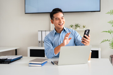 Business talk. Cheerful happy man using smartphone app for virtual communication, holding phone in hand for video call sitting at the desk in office.