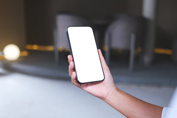 Mockup image of a woman holding and using mobile phone with blank desktop screen in cafe