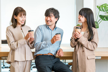 会社,オフィスでコーヒを飲みながら談笑するビジネスマンとビジネスウーマン
