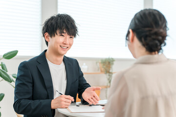 商談テーブルで女性顧客と打ち合わせ,カウンセリング,ヒアリングをする若いアジア人ビジネスマン
