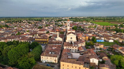 Aerial drone perspective capturing Pontevico's historic landscape, medieval church nestled among rolling countryside, dramatic clouded sky framing provincial Italian architecture