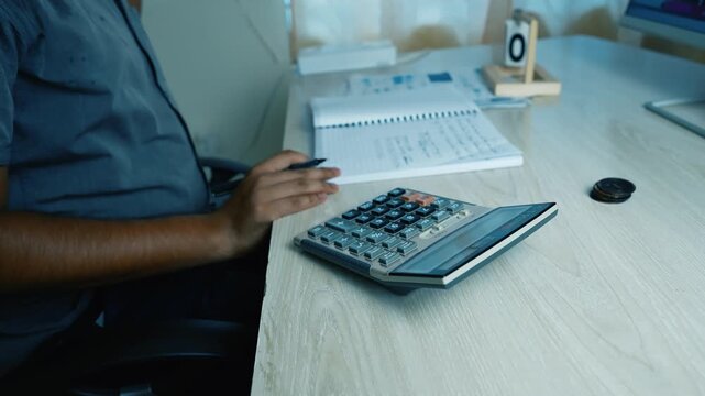 Person using a calculator at a desk with a notebook and computer