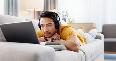 Man, laptop and headphones on sofa for movie, social media and video streaming or website in home. Relax, internet audio and male person on couch with technology, break and watching film on app