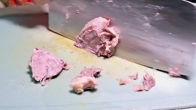 A cooked beef shank is being sliced on a cutting board with a sharp cleaver.