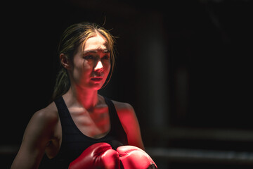 Young confident female Muaythai boxer guarding up on black background