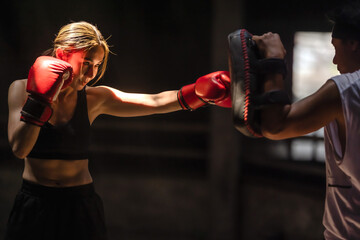 Confident female Muaythai boxer practicing Thai boxing with male trainer in gym