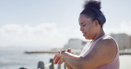 Plus size woman, smart watch and exercise in city with sky, break and check stats for weight loss by sea. Person, clock and stopwatch on ocean promenade with fitness, training and wellness in Brazil