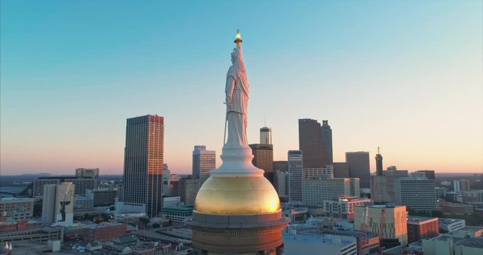 Aerial view of the Georgia State Capitol dome and statue of Freedom at sunset in Atlanta, USA. The sun is setting behind the buildings.