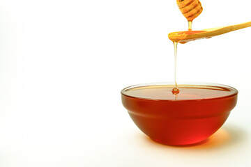 Honey is dripping from a honey dipper into a glass bowl on white background