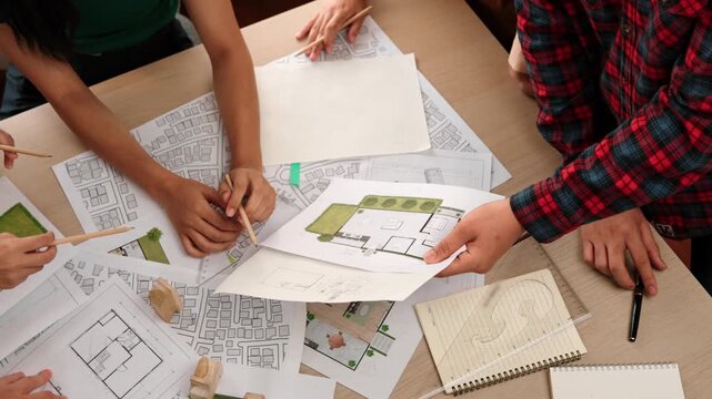 Smart architect and safety engineer discussion about building blueprint on table with architectural document, measurement tools and wooden block scatter around at modern office. Closeup. Delineation.