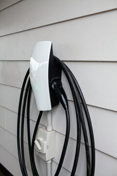 EV car charger plug and cable on side of white weatherboard home
