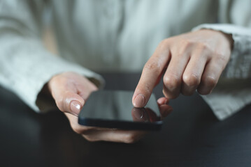 Close up of, woman sitting at wooden table using mobile phone in coffee shop, finger touching on phone screen. Woman using smartphone for mobile banking, online shopping, social media network
