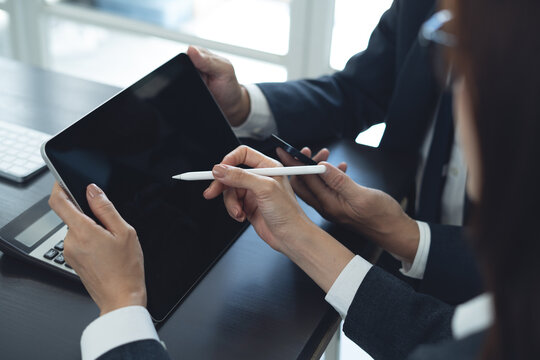 Businessman having a discussion with colleague, working together in office. Two asian business people using digital tablet at meeting. teamwork and collaboration - Powered by Adobe