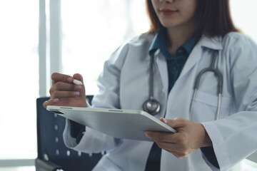 Asian female doctor using digital tablet examining online results of electronic health records in hospital, improved patient wellness and reading. Medical worker, digital technology