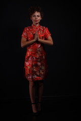 Full length portrait of young brunette woman in red dress on black background