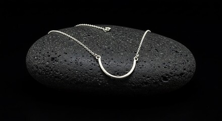 Mockup of minimalist silver curved bar necklace on dark textured stone against black background for commercial usage