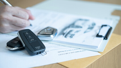 Closeup of car key and a hand writing on a document symbolizing vehicle sales contract signing and business transaction process