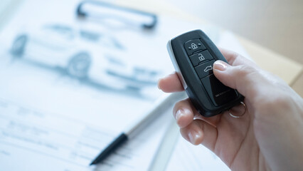 Car key in hand with paperwork and pen on table showing the automobile contract signing process and vehicle purchase concept